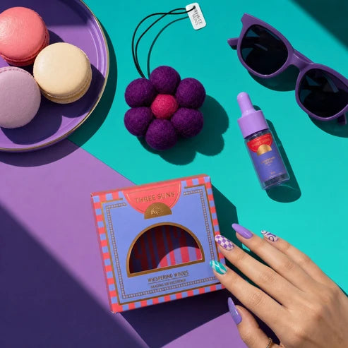 Colorful product display with a hand holding a box, macarons, sunglasses, and a bottle on a vibrant background.