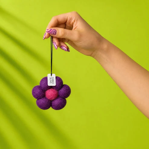 Hand holding a purple felt flower ornament against a green background