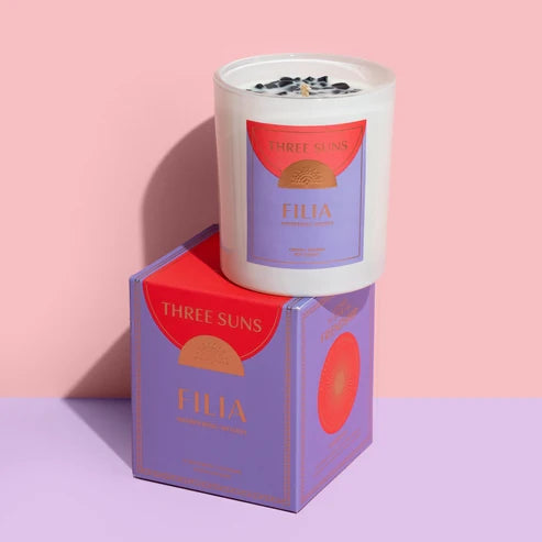A candle and box of Three Suns Filia candle on pale pink background