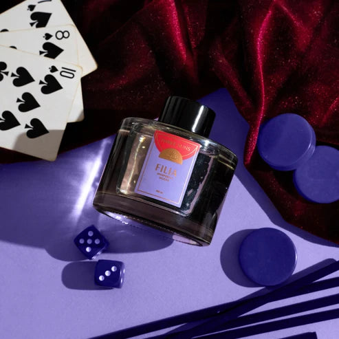 Glass reed diffuser bottle with a red label on a purple surface with playing cards and dice.