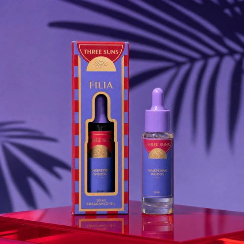 Three Suns Filia fragrance oil set, featuring a purple and red box alongside a matching dropper bottle on a reflective red surface against a purple background with palm leaf shadows.