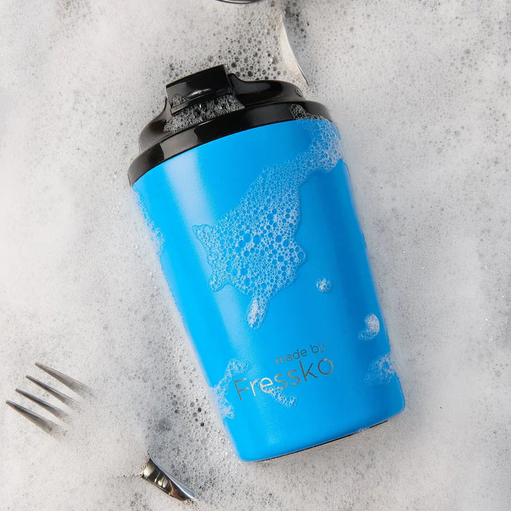 Blue travel mug with black lid in a sink with water &amp; bubbles