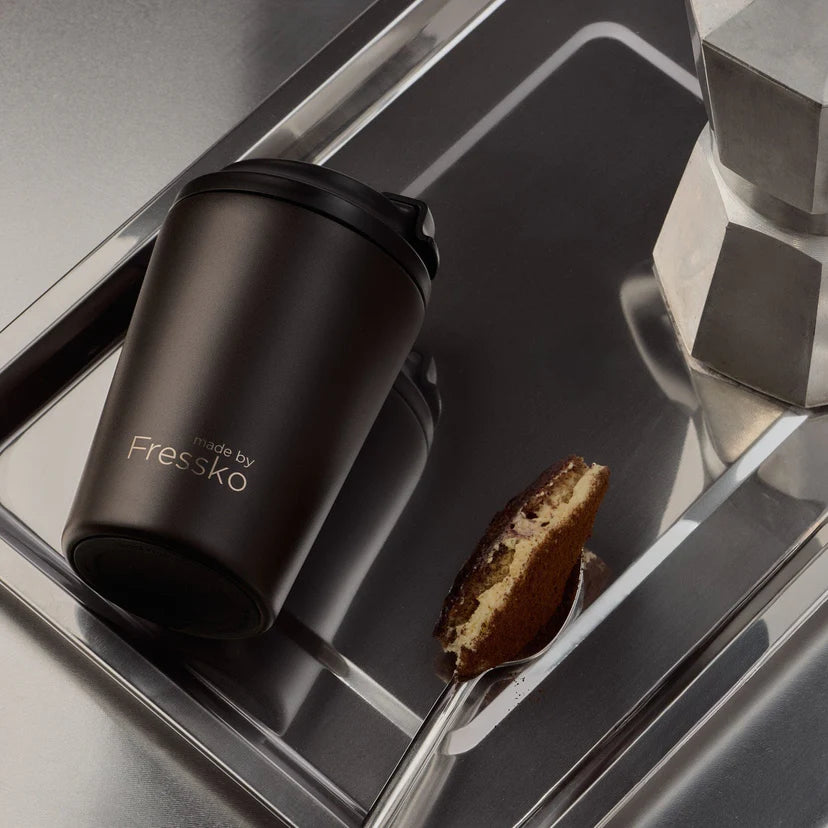 Brown Fressko mug on a reflective surface with a spoon and cookie