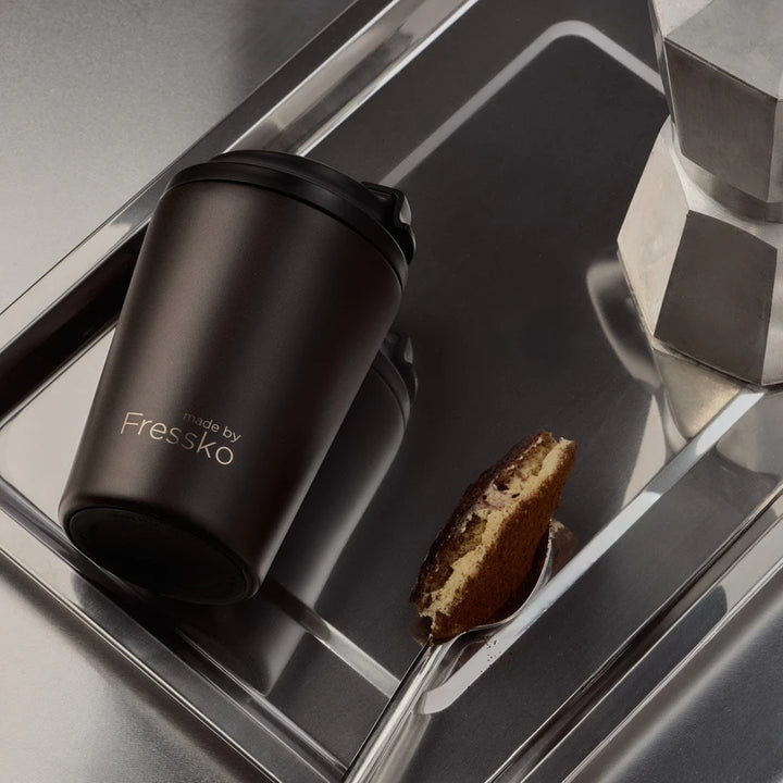 Brown Fressko mug on a reflective surface with a spoon and cookie