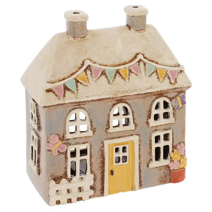 Decorative ceramic house tealight holder with a yellow door and colorful bunting on a white background