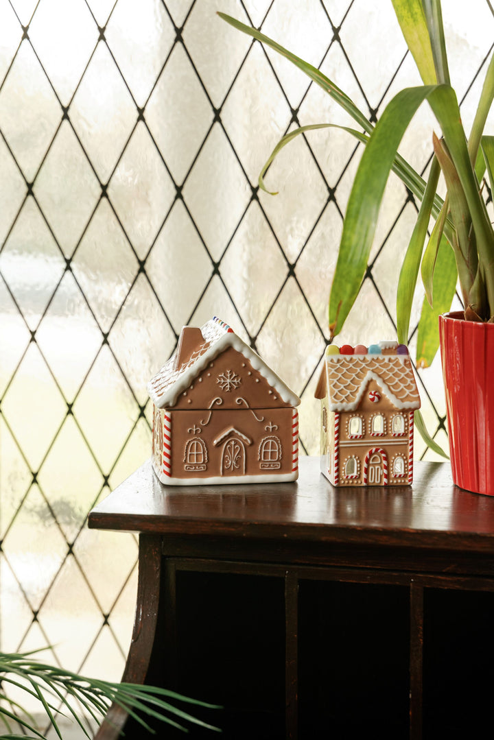 Two gingerbread house shaped ornaments on a table in front of a window