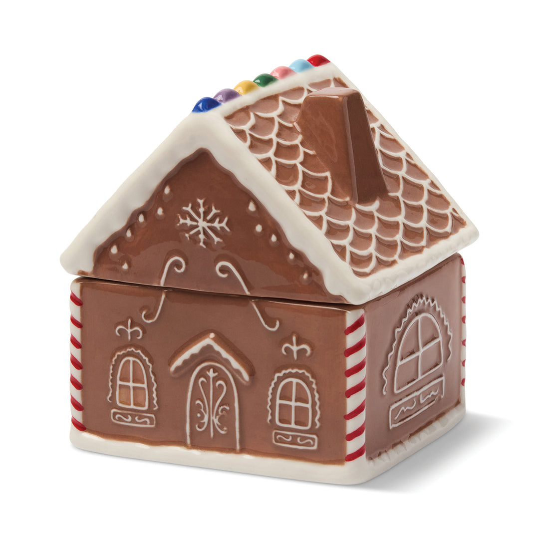 Gingerbread house-shaped candle with a white lid on a white background