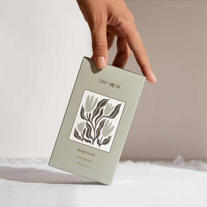 A hand holding a green box of stray Willow body scrub on a neutral background