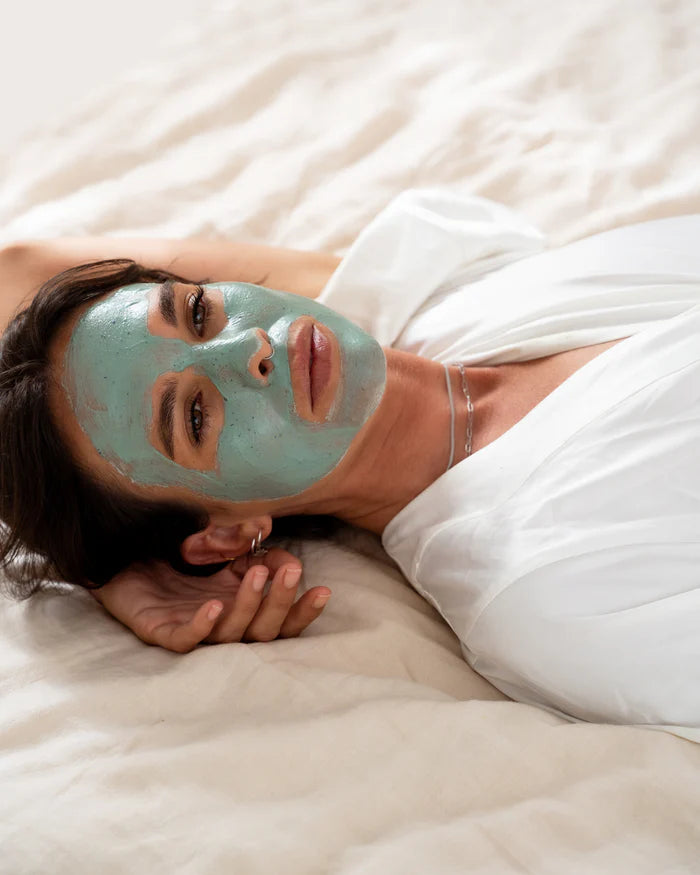 A woman laying on a bed with a green facial mask on 