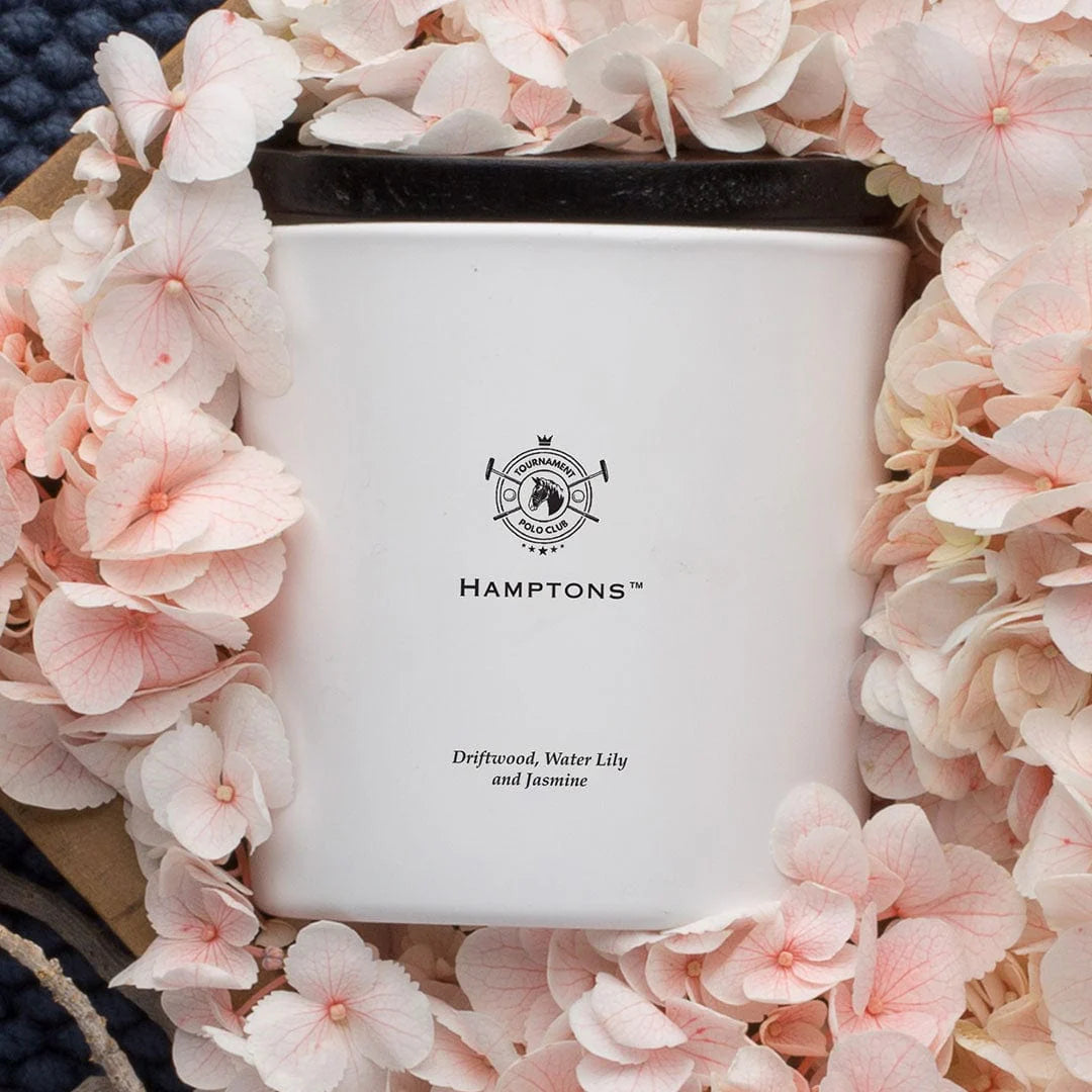 White candle with 'Hamptons' logo surrounded by pink flowers