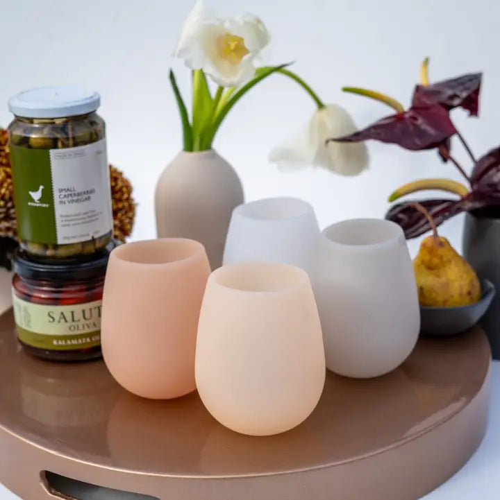 Four silicone tumblers on a table with jars and flowers in the background