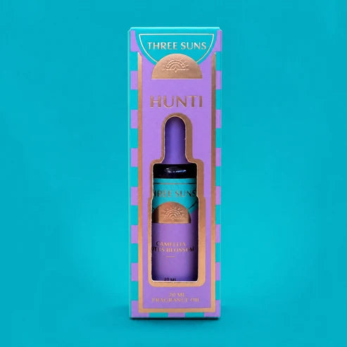 Three Suns Hunti fragrance oil  in a purple glass bottle, presented inside a decorative purple and teal gift box against a solid teal background.