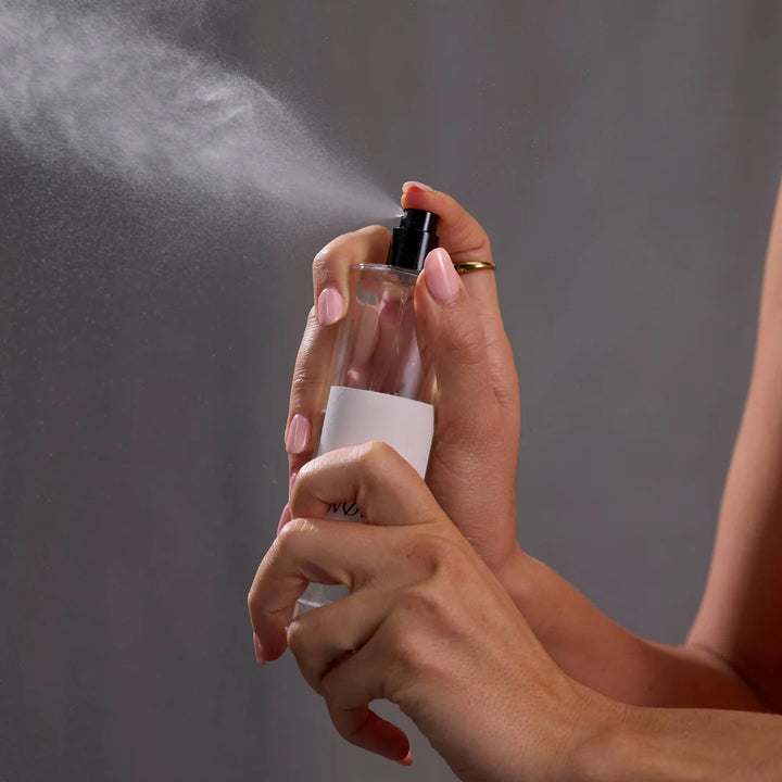 Person holding a clear spray bottle with mist against a gray background