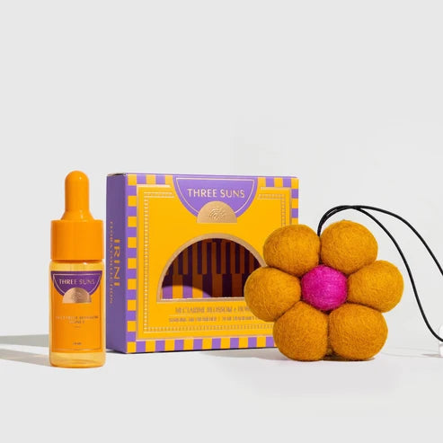 Three Suns gift set featuring a yellow and purple dropper bottle, a matching decorative box, and a yellow felt flower diffuser with a pink center and black cord, arranged on a light gray background.