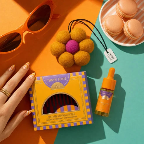 Three Suns product packaging with a hand, sunglasses, flower, and macarons on a colorful background