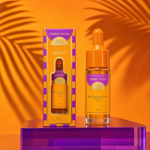 A bottle &amp; box of Three Suns Irini fragrance oil on a purple stand and an orange background