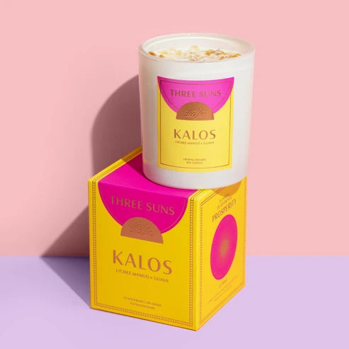 A Three Suns Kalos candle on a box with purple bench and pale pink background
