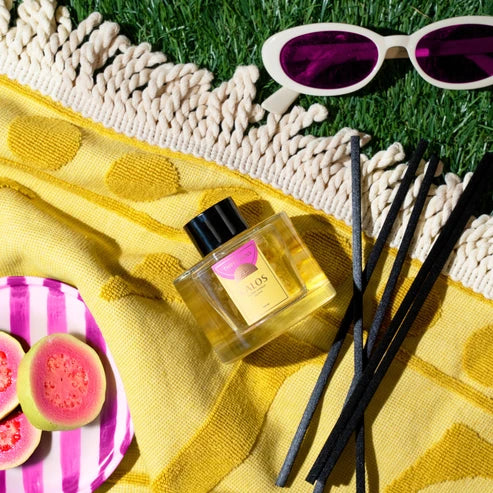 Diffuser with black sticks on a yellow towel with sunglasses and guava fruit in the background.