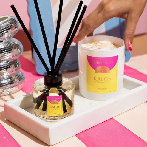 A hand with pink nail polish reaches toward a white candle labeled &