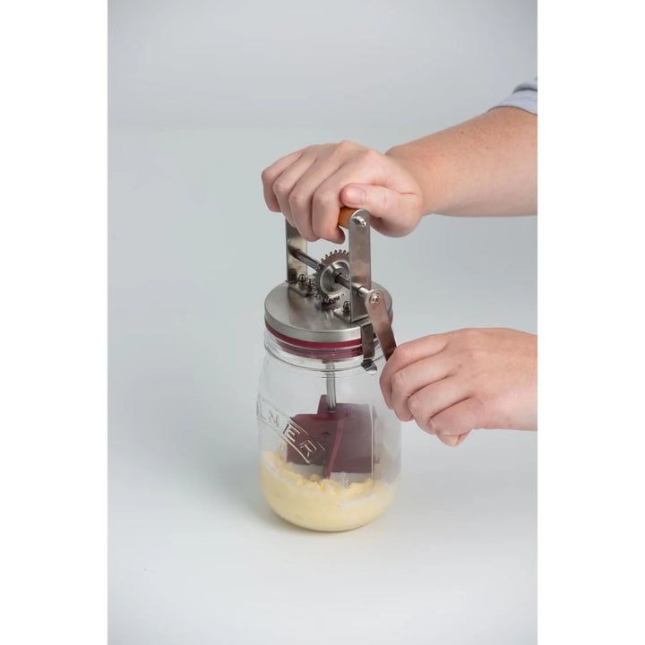 Person using a manual butter churner with a clear container on a light gray background