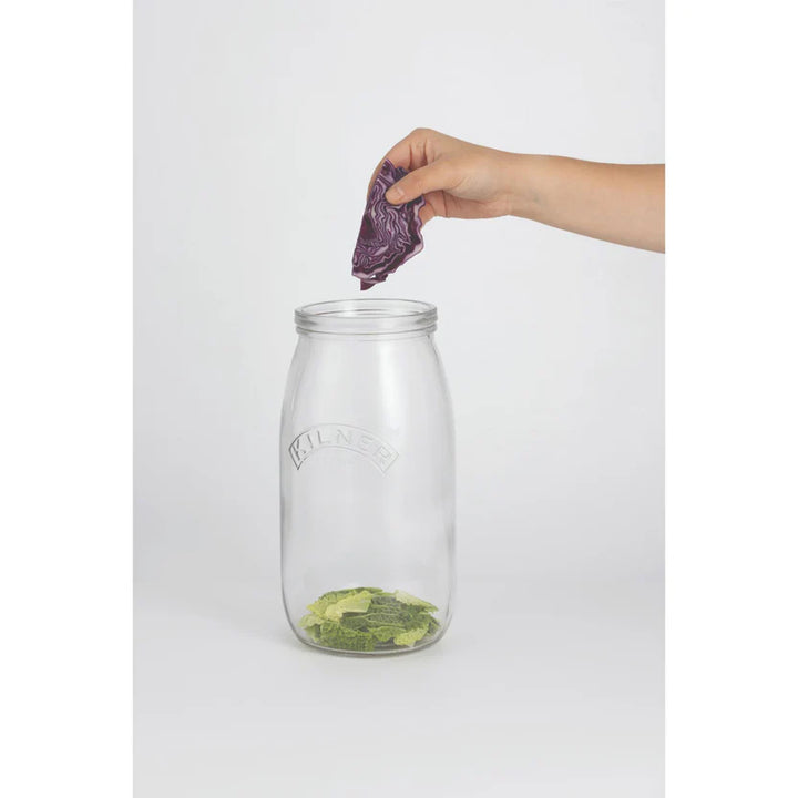 Clear glass jar with a hand placing purple cabbage inside on a white background