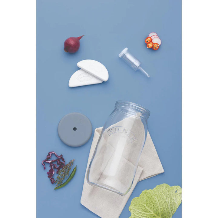 Collection of kitchen items including a fermenting jar, lid, and various vegetables on a blue background