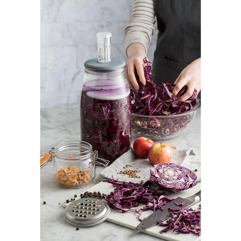Person preparing pickled red cabbage with a jar of liquid on a marble surface.