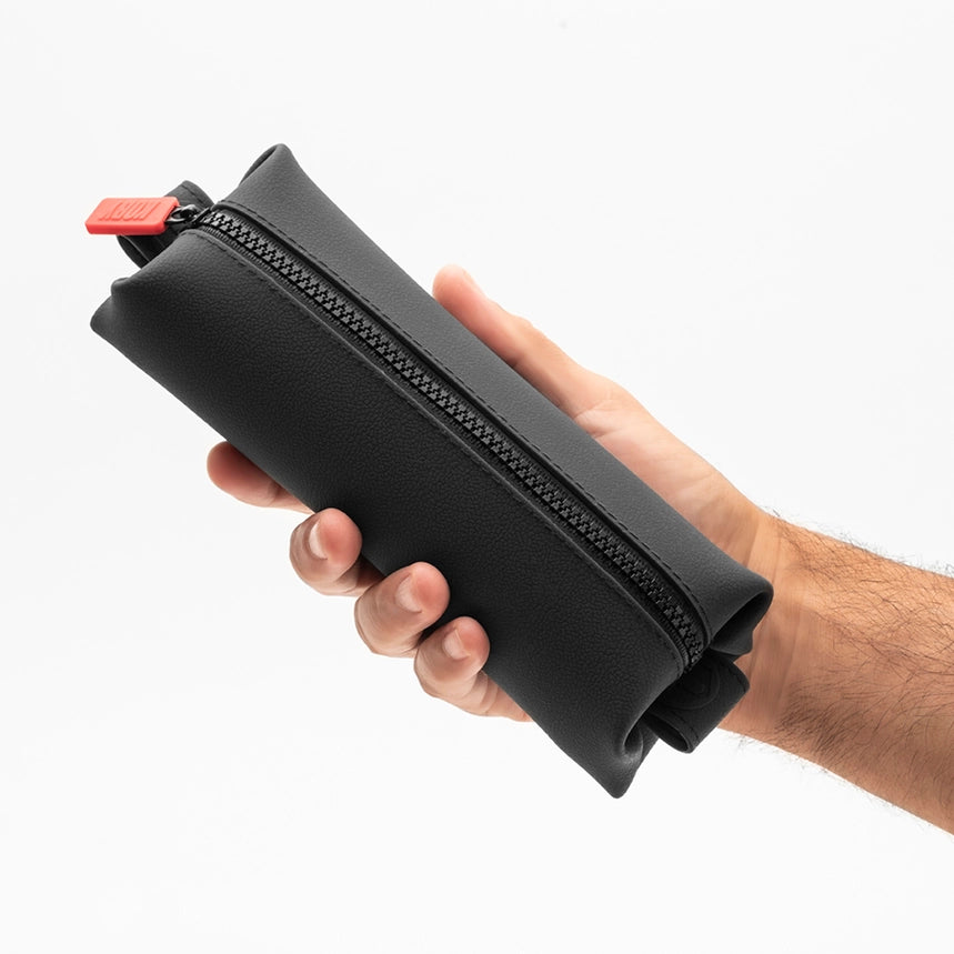 Hand holding a black zippered toiletry bag in front of a white background
