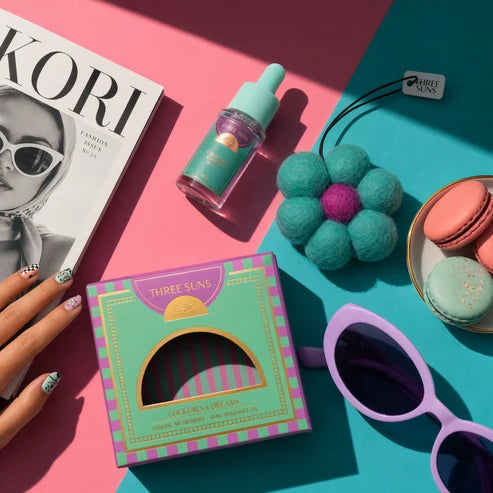Colorful product display with a magazine, bottle, box, sunglasses, and macarons on a pink and blue background.