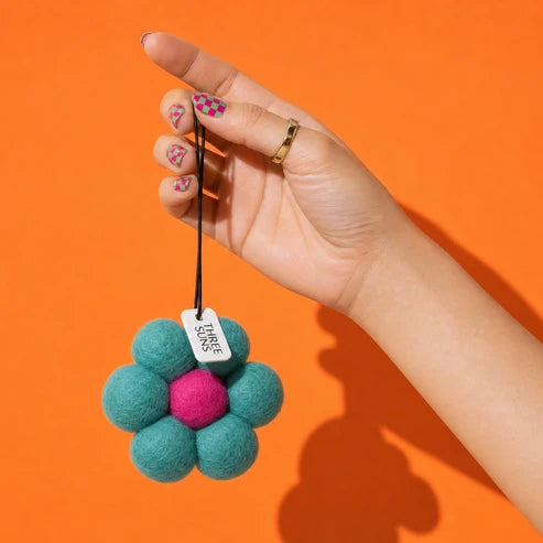 Hand holding a teal and pink flower-shaped air freshener against an orange background