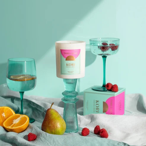 Candle with a box labeled 'Kobi' on a light blue surface with fruits and glasses.