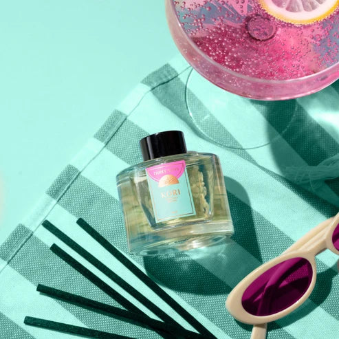 Clear bottle with black cap, pink label, and straw on a turquoise surface