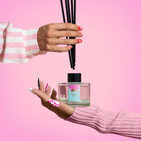 Hand holding a diffuser bottle with reeds against a pink background