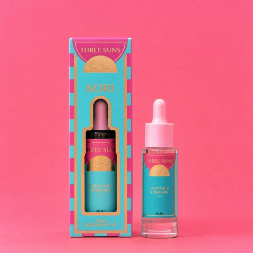 Three Suns Kori fragrance oil shown next to its colorful packaging box on a solid pink background.