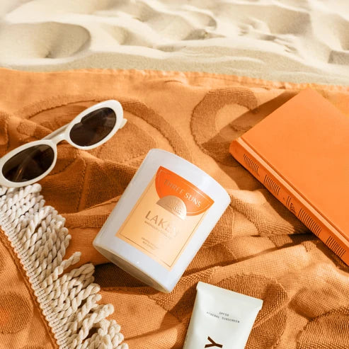 Sunscreen bottle, sunglasses, and book on an orange towel with sand in the background