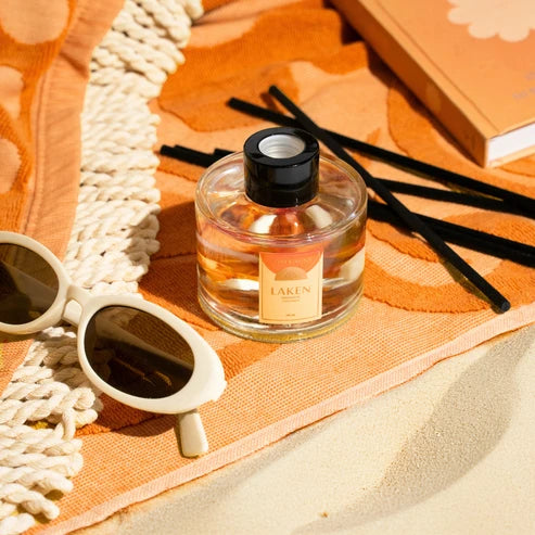 Perfume bottle with sunglasses and incense on an orange fabric background