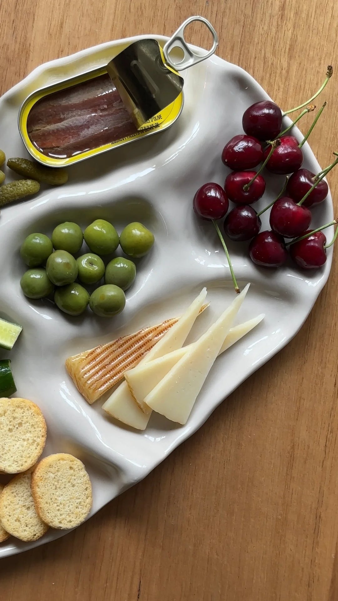 Assorted snacks including grapes, cheese, crackers, and cherries on a white tray.