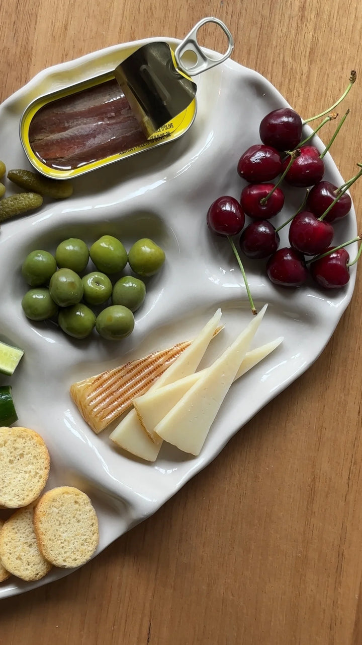 Assorted snacks including grapes, cheese, crackers, and cherries on a white tray.