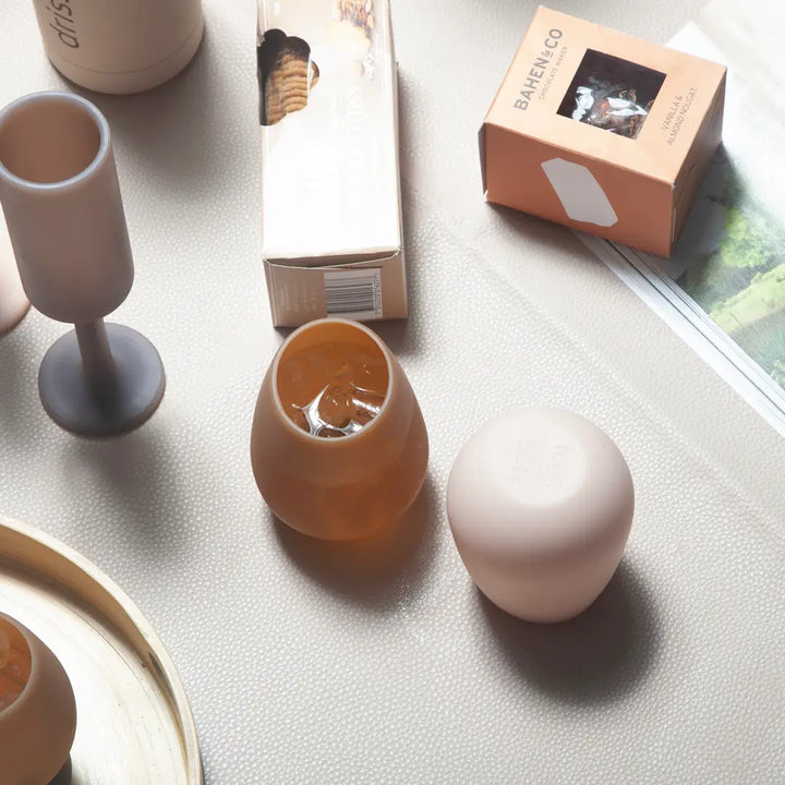 A styled flat-lay of silicone glassware and packaging on a textured light gray surface.