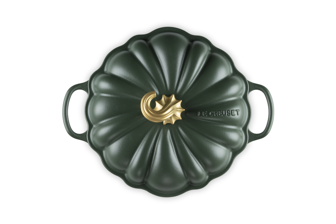 A Le Creuset enameled cast iron Dutch oven with a lid, shown from a top-down perspective. The pot has a dark forest green pumpkin-inspired ribbed lid with two side handles and a central gold-tone decorative emblem.
