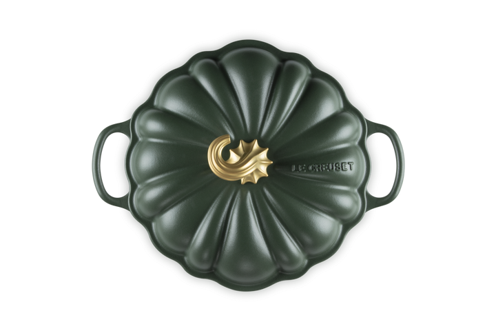 A Le Creuset enameled cast iron Dutch oven with a lid, shown from a top-down perspective. The pot has a dark forest green pumpkin-inspired ribbed lid with two side handles and a central gold-tone decorative emblem.