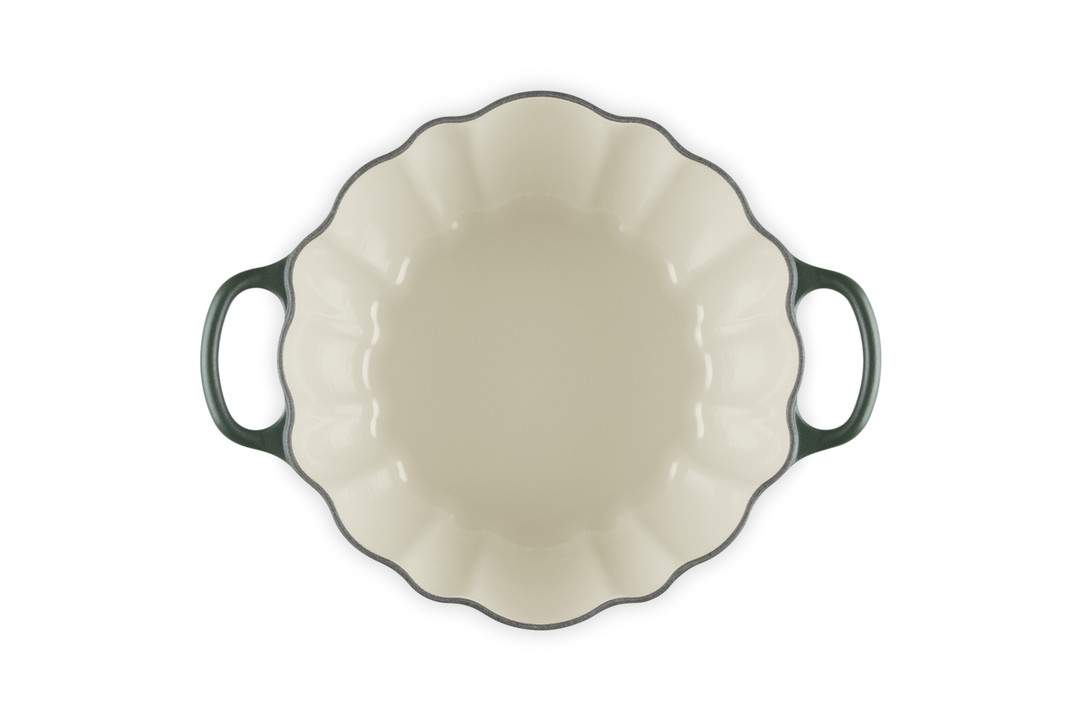 An oval enameled cast iron casserole dish viewed from directly above, featuring a cream-colored interior, a dark green rim, and dark green handles on a solid white background.