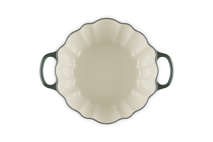 An oval enameled cast iron casserole dish viewed from directly above, featuring a cream-colored interior, a dark green rim, and dark green handles on a solid white background.