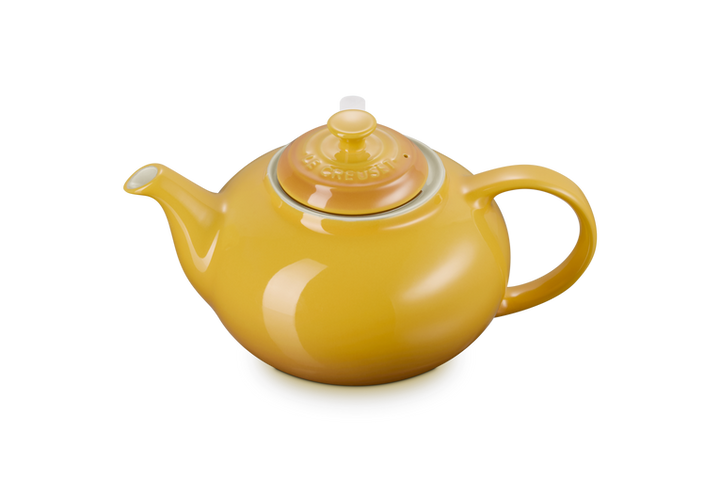 Yellow Le Creuset teapot on a white background