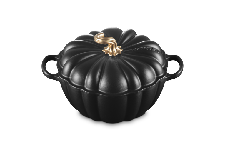 A black cast iron pumpkin-shaped lidded casserole dish with side handles and a decorative gold-toned stem on the lid, shown on a plain white background.