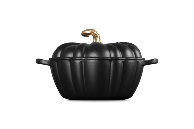 A black cast-iron Dutch oven shaped like a pumpkin with a textured finish, featuring a gold-colored handle and lid knob, set against a solid white background.