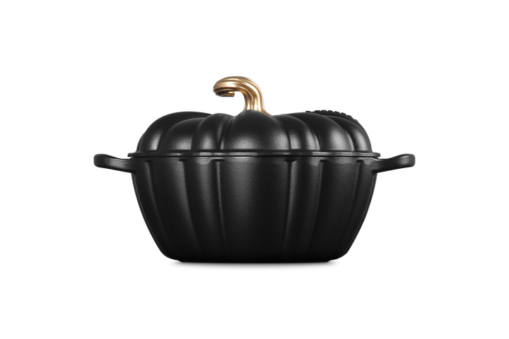 A black cast-iron Dutch oven shaped like a pumpkin with a textured finish, featuring a gold-colored handle and lid knob, set against a solid white background.