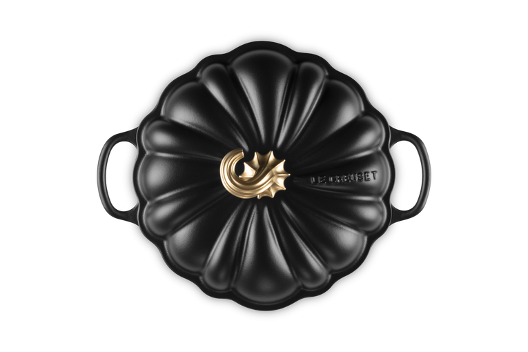 A black cast iron Dutch oven with a lid designed in a pumpkin shape, featuring a polished gold-toned metal central knob and the &