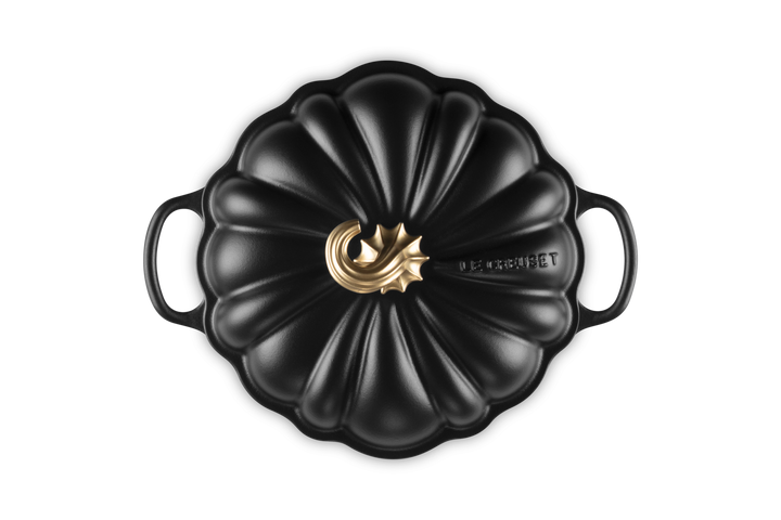 A black cast iron Dutch oven with a lid designed in a pumpkin shape, featuring a gold-toned metal central knob and the &