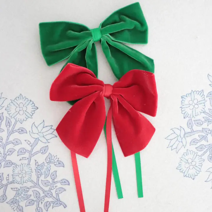 Two velvet ribbon bows, one green and one red, displayed on a white background with faint blue floral line drawings.
